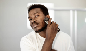 Young Black man using hair clippers to trim his beard.